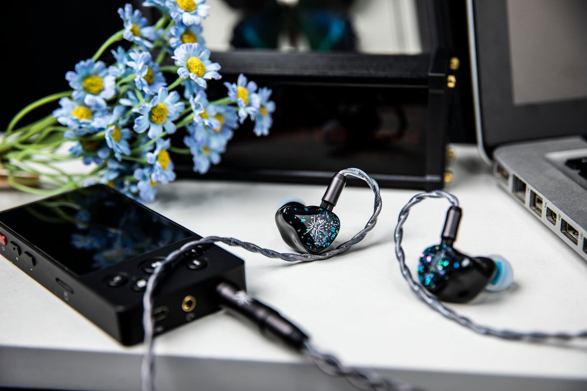 Kiwi Ears Astral plugged into a black music player on a desk, with blue flowers and a laptop behind